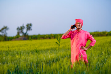 Young indian farmer talking on smartphone at wheat field