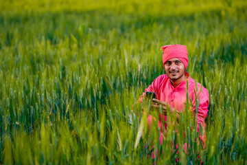 Young indian farmer using smartphone at wheat field