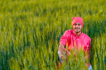 Naklejka na ściany i meble Happy young indian farmer at green wheat field