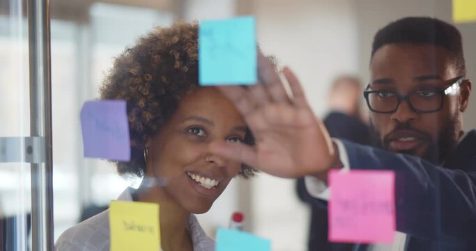 African business people brainstorming putting sticker notes on glass board at modern office