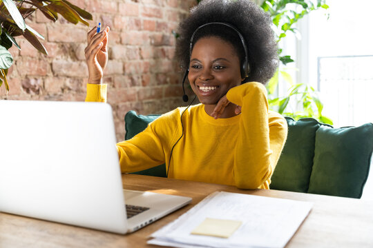 Smiling Afro-American woman employee wear headphones, talking on zoom with clients on laptop, consulting customer, giving online educational class lecture, watching webinar at home office.