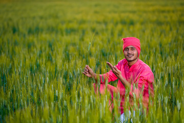 Happy young indian farmer at green wheat field