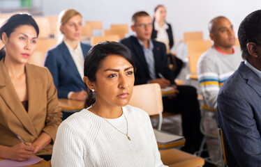Concentrated latin american woman attentively listening to lecture with colleagues at business...
