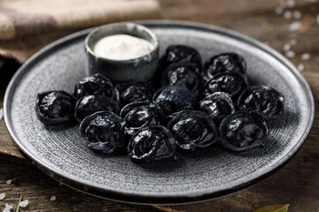 Traditional Russian dumplings, painted with cuttlefish ink for black dough. Still life on a wooden board. Close-up.