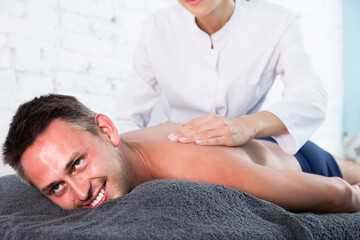 Obraz na płótnie Canvas happy english female masseur doing massage at back man who lying on a massage table in a beauty salon