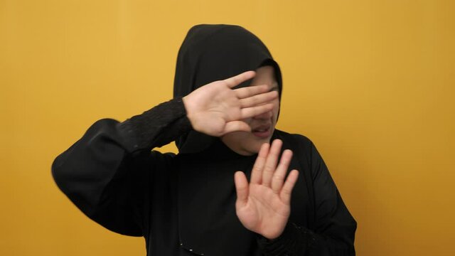 Beautiful Asian musim woman afraid expression with hands raised up, surrender gesture, over yellow background