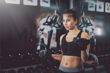 Fototapeta na wymiar Asian woman in sportswear Be determined in exercise By lifting dumbbells at the gym