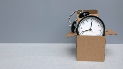 An alarm clock on a brown box on a grey background with copy space.