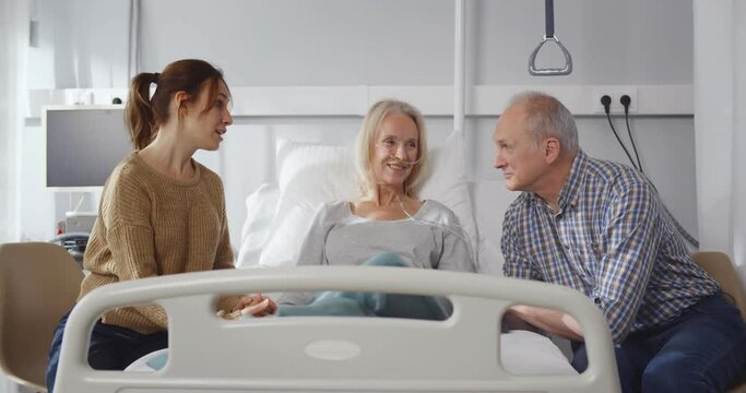 Senior woman lying in hospital bed getting visit from family
