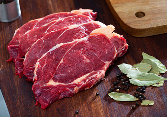 Piece of beef with peas of bitter pepper and laurel leafs on dark broun cutting board