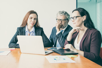 Obraz premium Group of professional watching presentation on computer, sitting at meeting table with charts in documents Medium shot. Marketing and teamwork concept