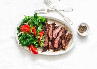 Beef steak and kale, tomato salad - delicious balanced diet lunch on a light background, top view