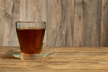 Glass cup of tea with saucer on wooden table. Copy space