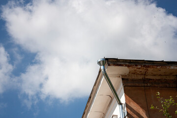 A roof corner of a house with a funnel. Bottom view of the corner of the roof of a house against the backdrop of white clouds in the sky. The sun illuminates the corner of the roof of the house.