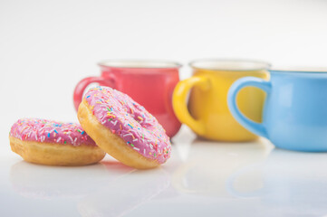 Tasty donut with colorful cups of coffee on white background