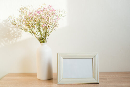 Horizontal white frame mockup on vintage wooden bench, table. Modern white ceramic vase gypsophila. White wall background.