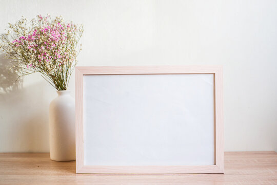 Horizontal white frame mockup on vintage wooden bench, table. Modern white ceramic vase gypsophila. White wall background.