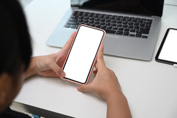 Close up view of young girl using mobile phone while sitting in front of her laptop computer at home.