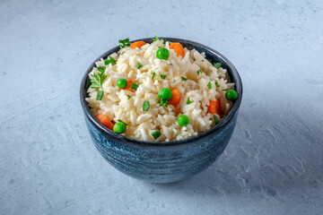 Rice with vegetables. White rice with green peas, carrots, and scallions, in a blue bowl