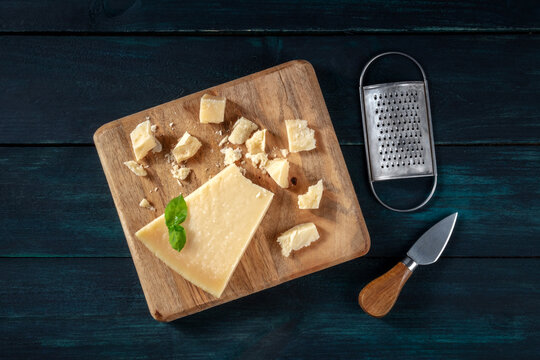 Crumbled Parmesan Cheese With Basil, A Knife, And A Grater, A Flat Lay Overhead Shot On A Dark Wooden Background