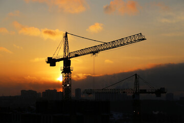 Silhouettes of construction cranes and unfinished residential buildings on sunrise background. Housing construction, apartment block in winter city