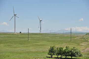 Fototapeta premium Zhambyl region, Kazakhstan - 05.15.2013 : Wind turbines located in an open hilly area with trees and grass