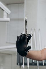 a dentist wearing black gloves holds a metal syringe in his hand