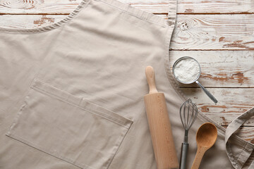 Apron, utensils and flour on wooden background, closeup