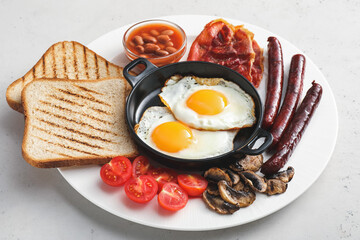 Traditional English breakfast with fried eggs in plate on light background