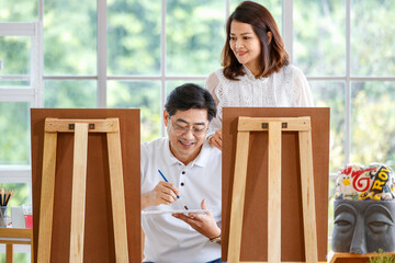 Senior man and woman couple, husband and wife, painting image together in home gallery with warm...