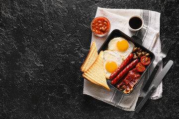 Traditional English breakfast with fried eggs in pan on dark background