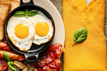 Traditional English breakfast with fried eggs in plate on wooden background