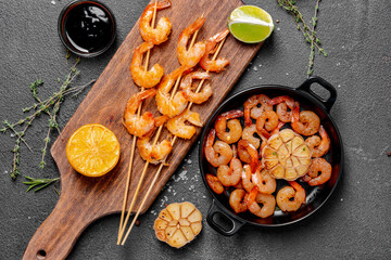 Frying pan and board with tasty shrimps on dark background