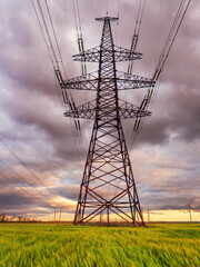 High-voltage power lines passing through a green field, on the background of a beautiful cloudy sky