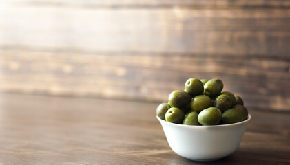 Green olives in a white plate on the table. On a wooden background