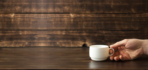 White cup for coffee in hand. On a wooden background
