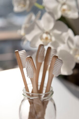 Close-up of bamboo toothbrushes in a glass with flowers in the background
