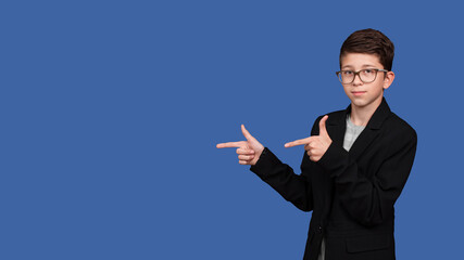 beautiful boy with glasses, pointing his hands to empty place isolated on blue background. copy space. 