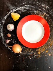 Fototapeta na wymiar a white and red round plate on a black table decorated with spices.