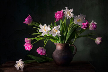 Classic still life with beautiful white and pink tulip flowers bouquet in vintage clay jar. Art photography.