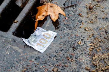 Money. American one hundred dollar bill on the edge of a storm drains grate after rain.