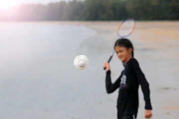 An Asian girl was playing badminton on the beach with her brother.
