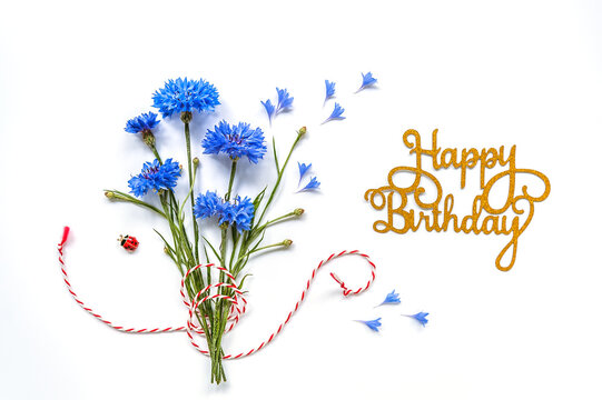 Happy birthday concept. Bouquet of delicate cornflowers on white background with red and white rope. Soft focus, copy space. Flat lay, top view.