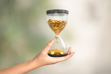 Hourglass with gold coins on hand, Time is money concetp