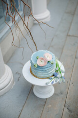 Wedding cake with soft blue cream and decorated with fresh flowers on a white stand.