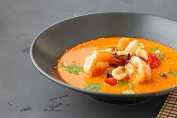 Tom Yam Thai soup in black bowl on gray table