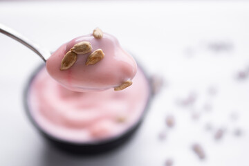 Strawberry yogurt with sunflower seeds on spoon with strawberry yogurt in black cup blured. food for health concept.