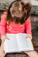 Baby girl in a red on green grass and reading a book in a sunny summer day