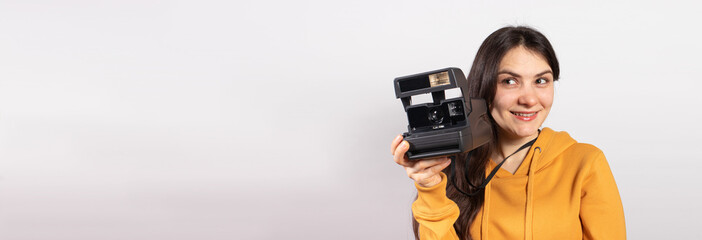 Beautiful lady brunette holds a camera and takes pictures, smiling on a white background. Female photographer, courses and photography training. Banner with copy space for text.