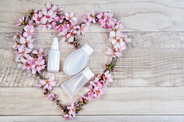flower heart with a cream and a bottle of antiseptic spray on a wooden surface. valentine's day gift. Spring holidays. Flowers and branches of almond tree. Cosmetics set for treveling.Presentation..